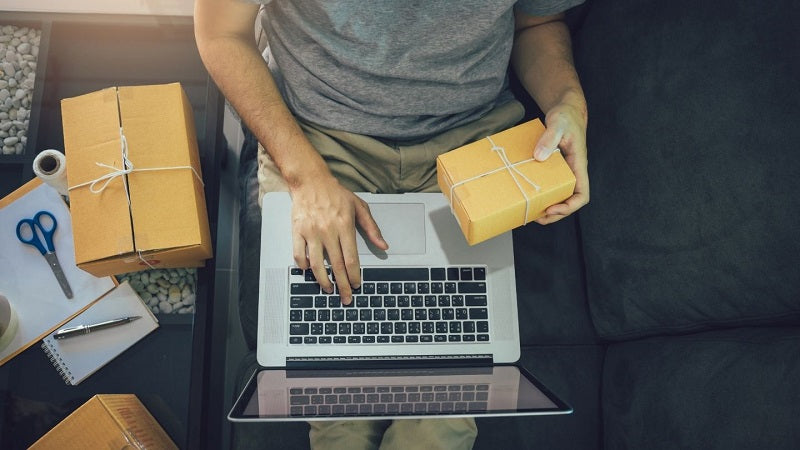 Hombre en su computador y tiene un paquete en la mano.