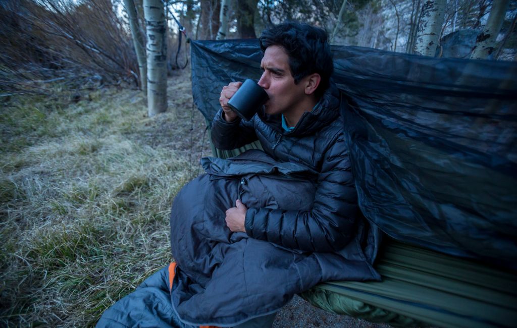 hiker sipping coffee while using a hammock underquilt