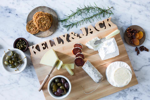 Maple Wood Cutting Board with names Kelly & Jack cut out on the top. The board has a mix cheeses, olives and meats.