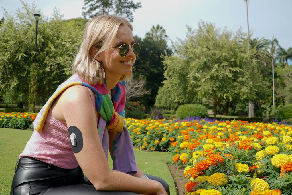 Sophia kneeling in flower garden with black dexcom patch on arm