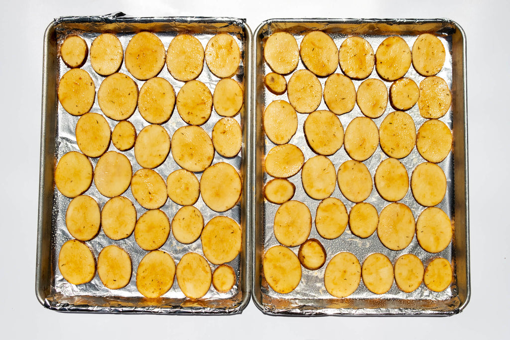 Sliced and seasoned potatoes layered on baking sheet