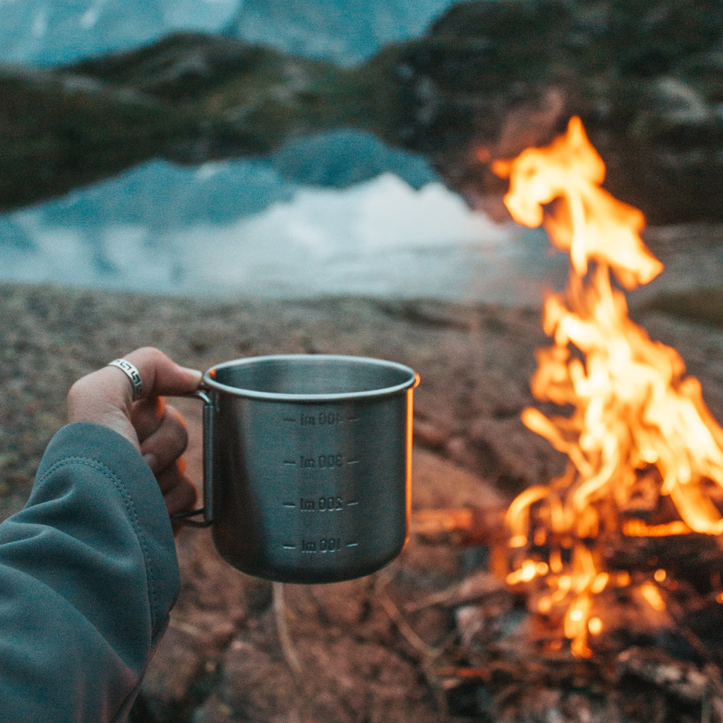 Someone holding a metal mug in front of a campfire