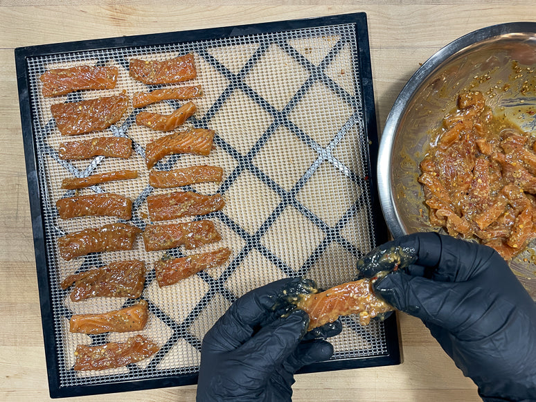Laying the marinated salmon jerky onto screens.