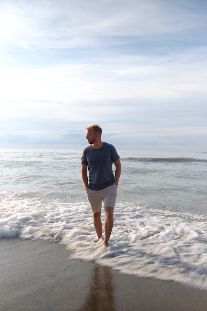 Man walking along pebbly beach in waves