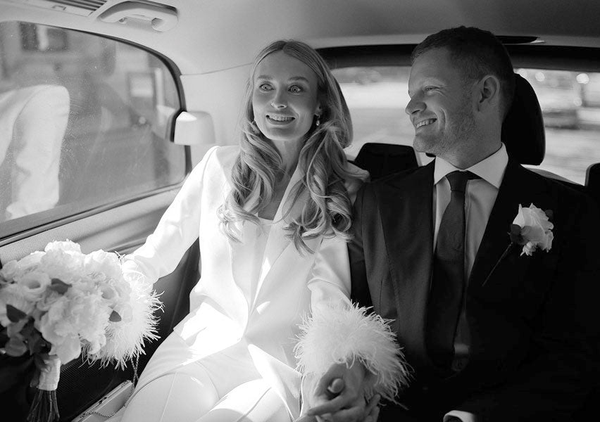 Bride and groom smiling in car holding a wedding bouquet