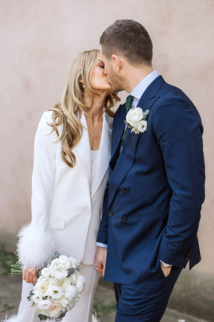 Bride and groom kissing and bride holding a white classic wedding bouquet with peonies and roses