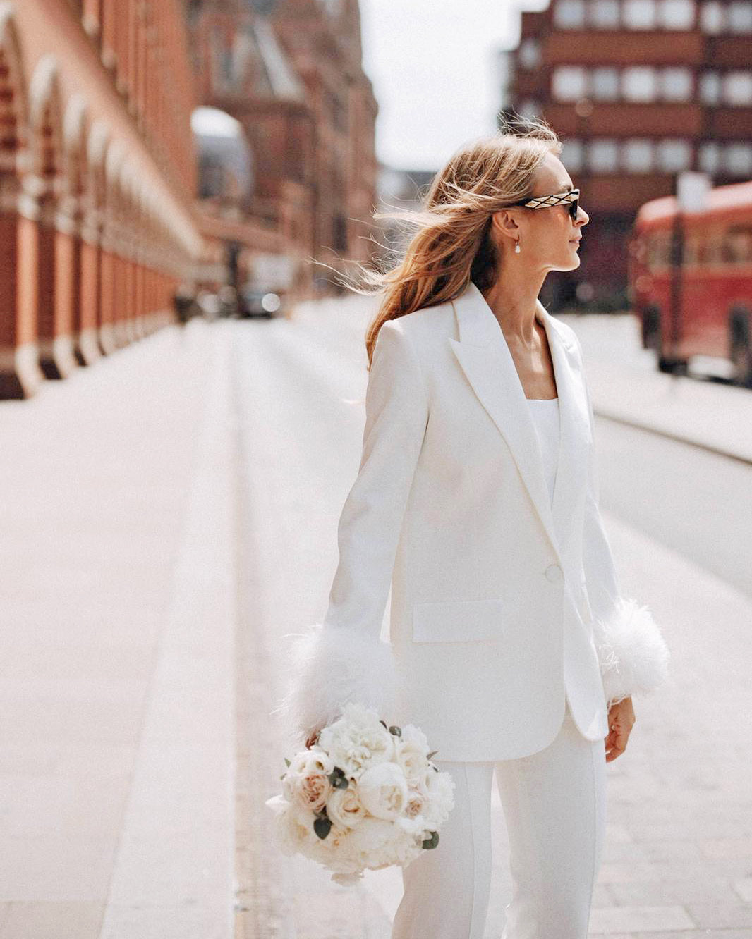 Modern chic bride in white suit holding classic bridal bouquet with peonies and white roses