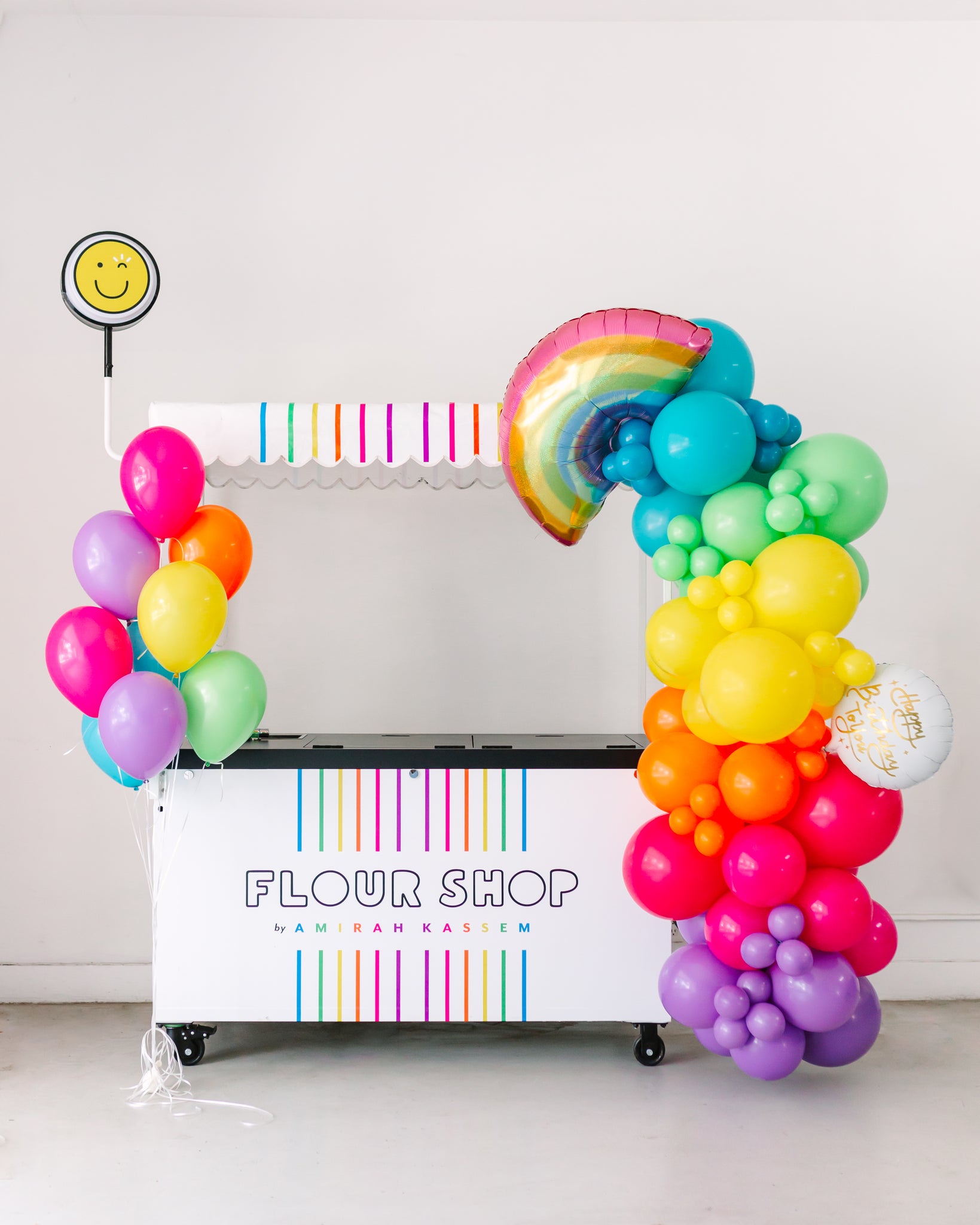 Flour Shop cart with a Bonjour Fête rainbow balloon garland.