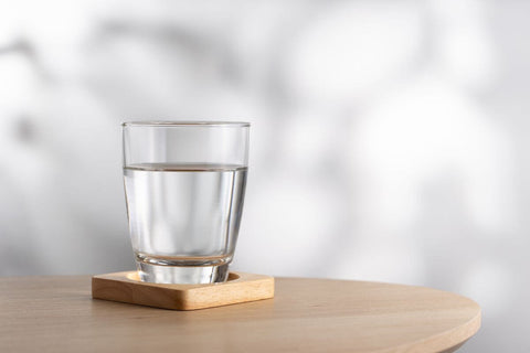 water in a glass on a wooden coaster sitting on a wooden table as an alternative to dishwasher detergent