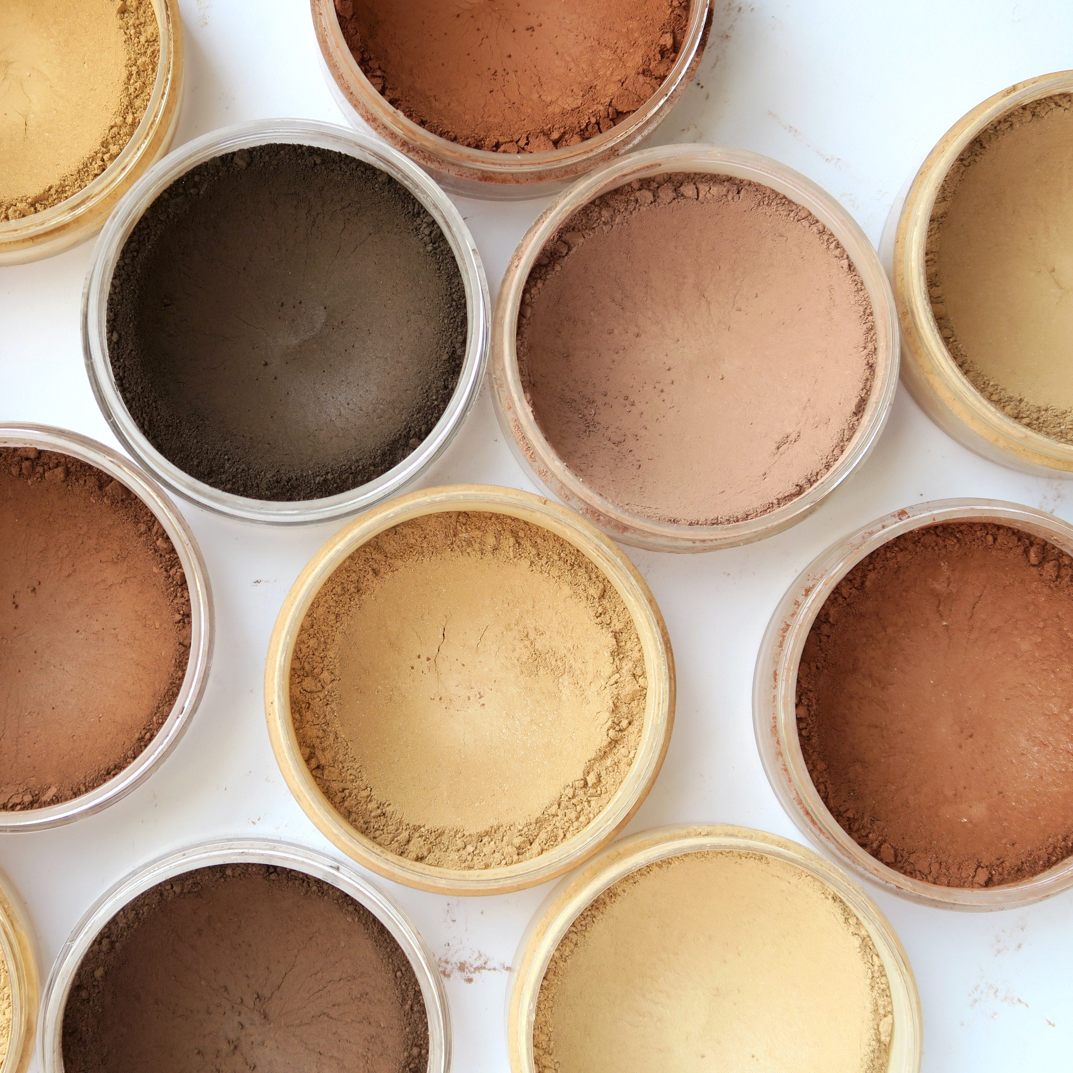 Various shades of loose powder makeup in round containers arranged on a white surface.