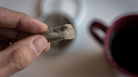 male fingers holdinga pouch of portioned snus with a coffee mug in the background