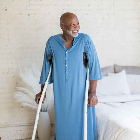 Handsome smiling middle-aged man wearing ocean blue hospital gown on crutches with foot brace