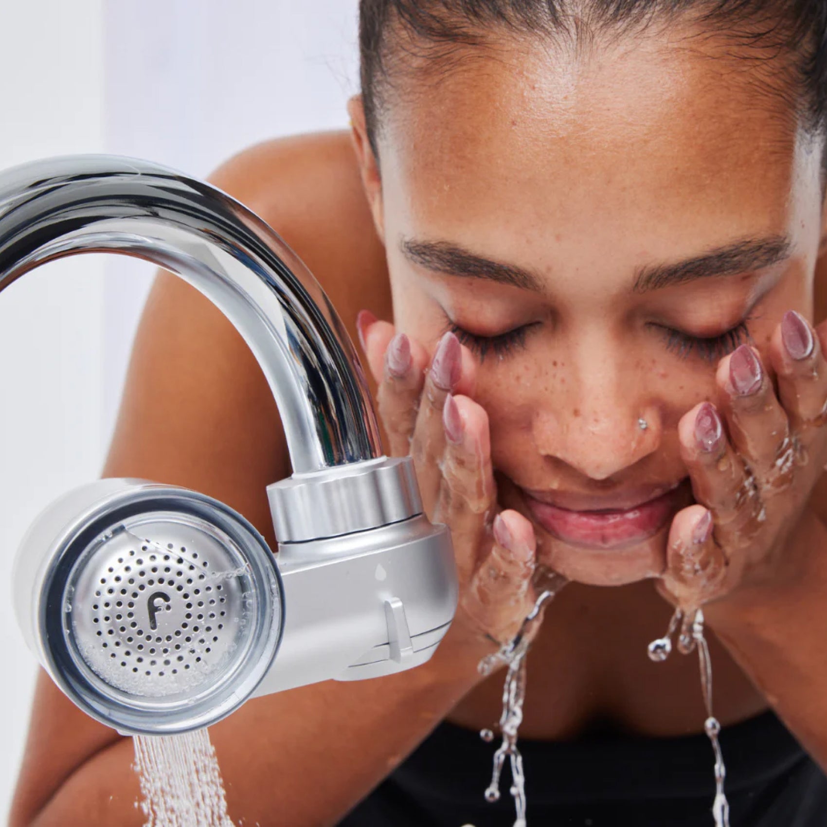 Woman washing face under a running faucet.