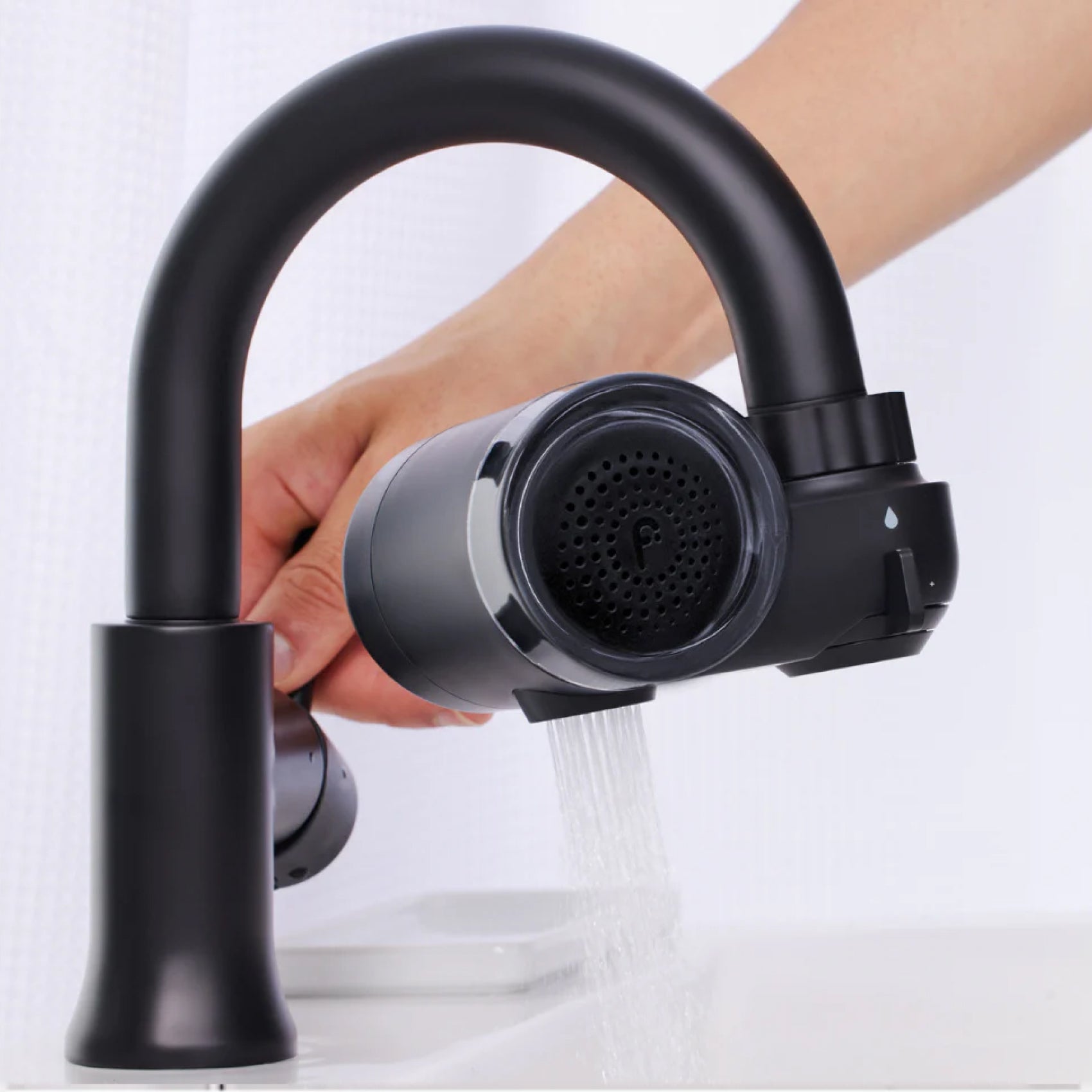 Hand holding a detachable black kitchen faucet head with water running.