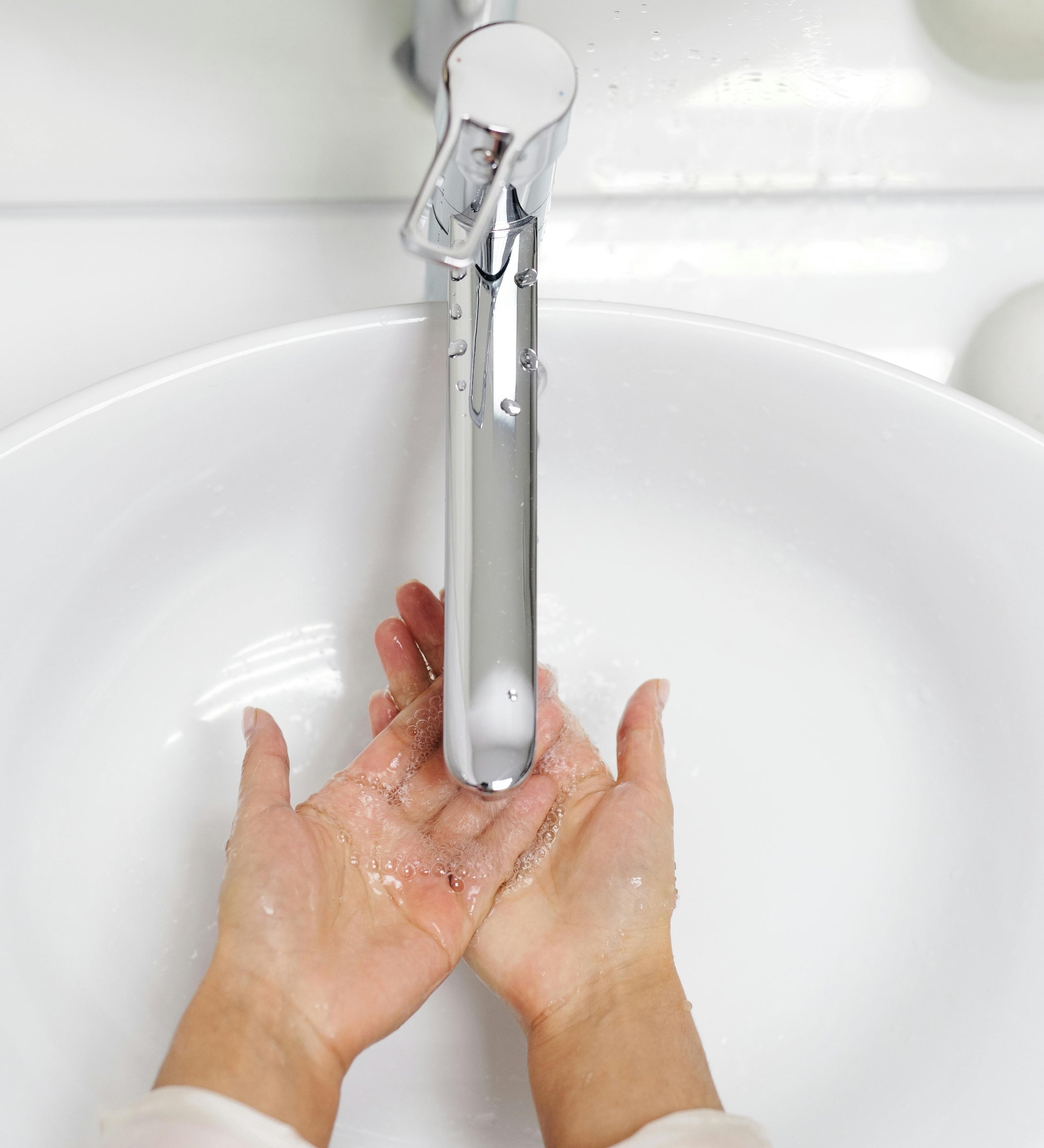 Hands being washed under a modern silver faucet in a white sink.