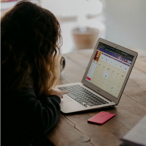 adolescent girl sits at wooden table working on a laptop