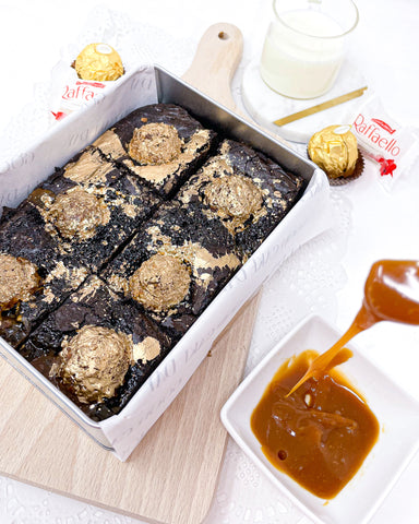 Dripping Caramel sauce beside Ferrero Rocher brownies in an airtight brownie tin