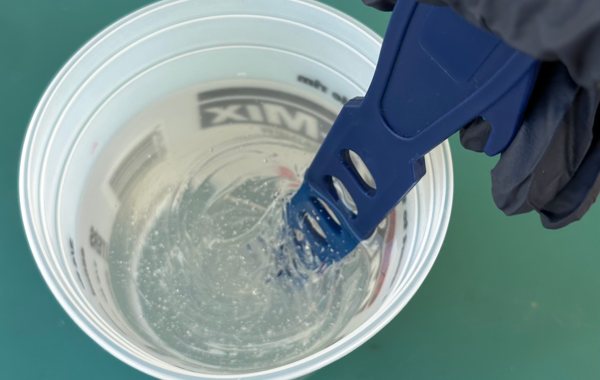 A small epoxy batch being carefully mixed in a mixing container with measuring lines.