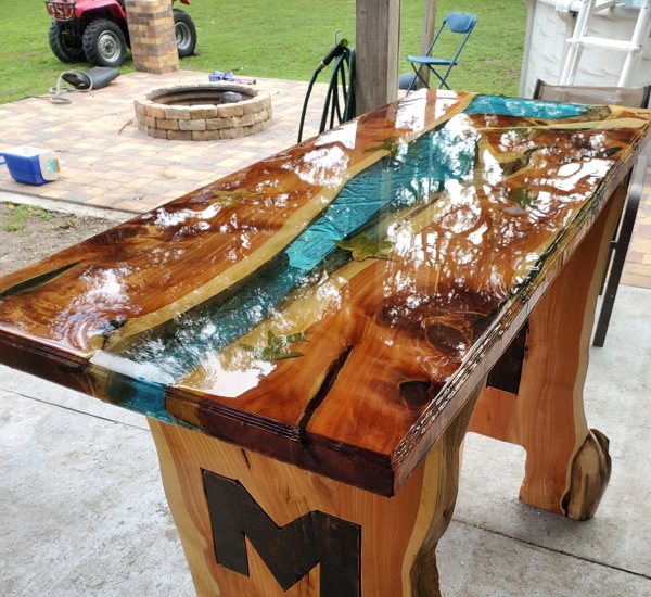 A wooden epoxy river table, with a thick blue-tinted river vein.
