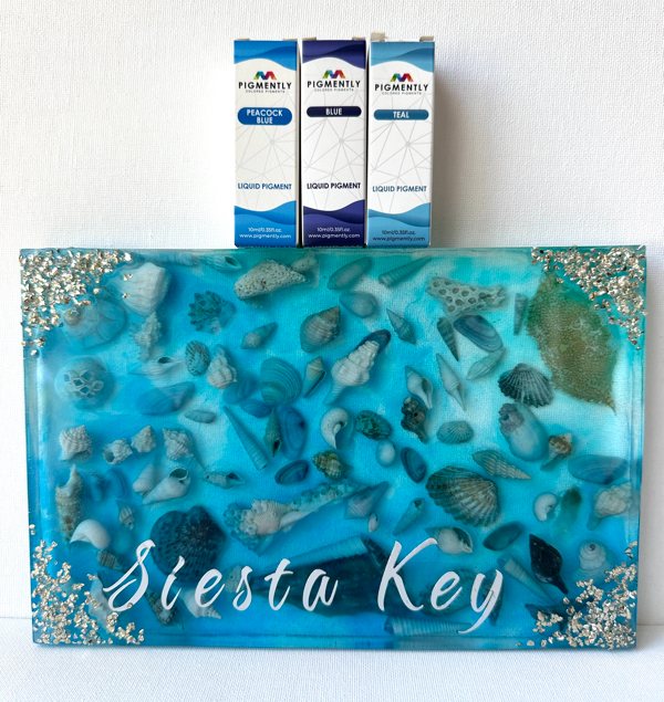 A sea-themed resin art piece made with Primaloc Epoxy Resin, seashells collected from a beach, and three different blue-toned Pigmently pigments.