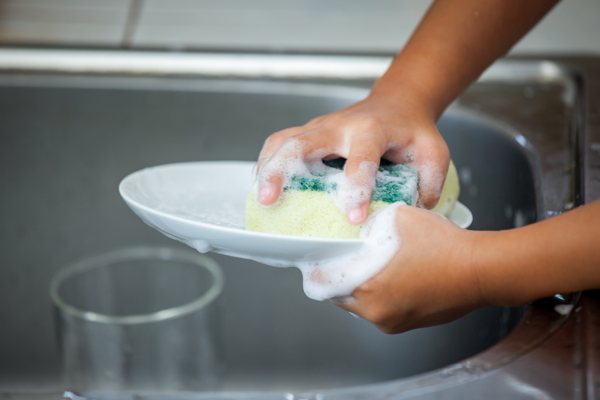 A youth cleaning a used dish with a sponge and soapy water.