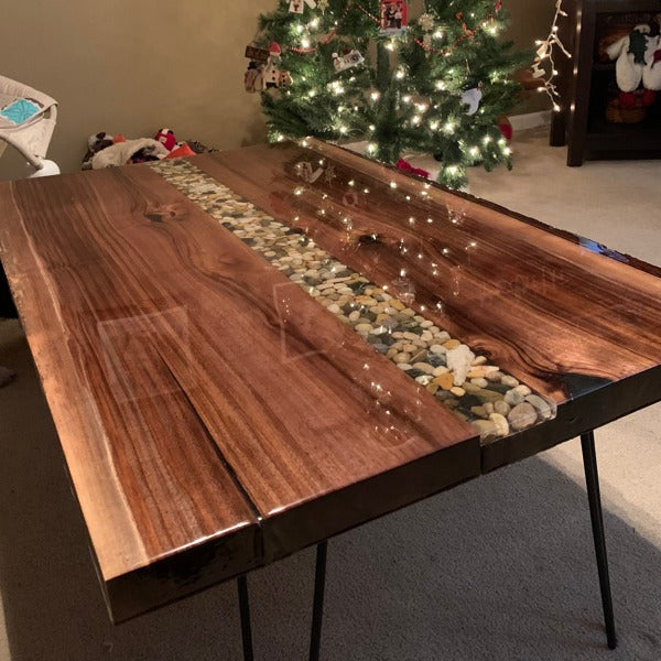 A long wooden epoxy coffee table with a river vein of epoxy that contains numerous embedded stones.