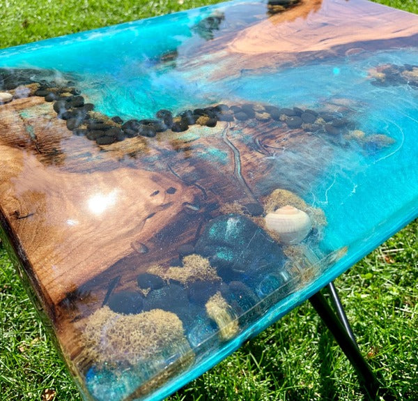 A sea-themed epoxy table top with various sea embedments and a brilliant blue resin tint..