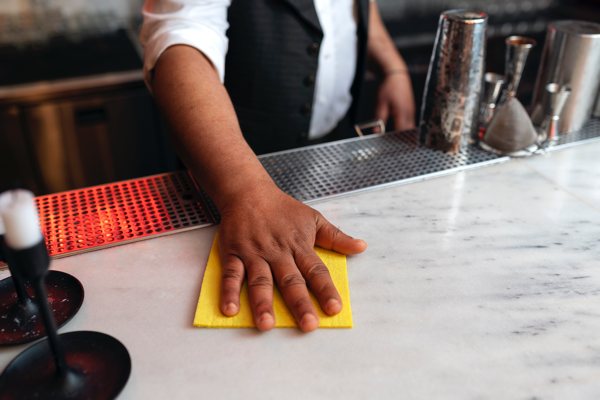 A photo of a man cleaning an epoxy bar top in a commercial bar room.