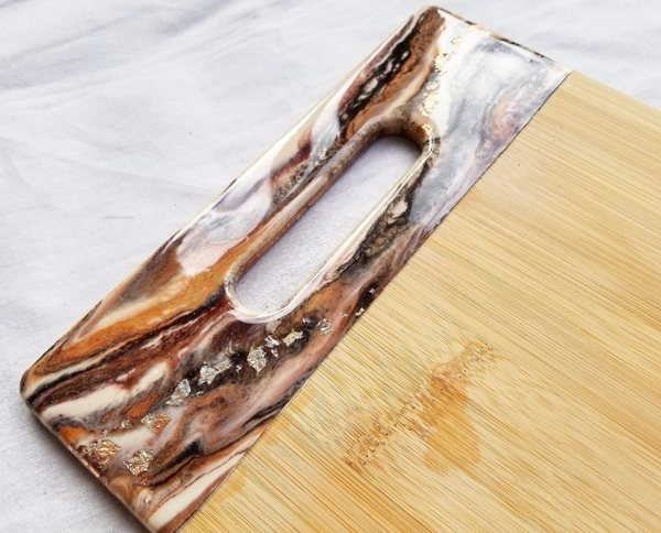 A wooden cutting board with a colorfully tinted epoxy resin accept around the handle.