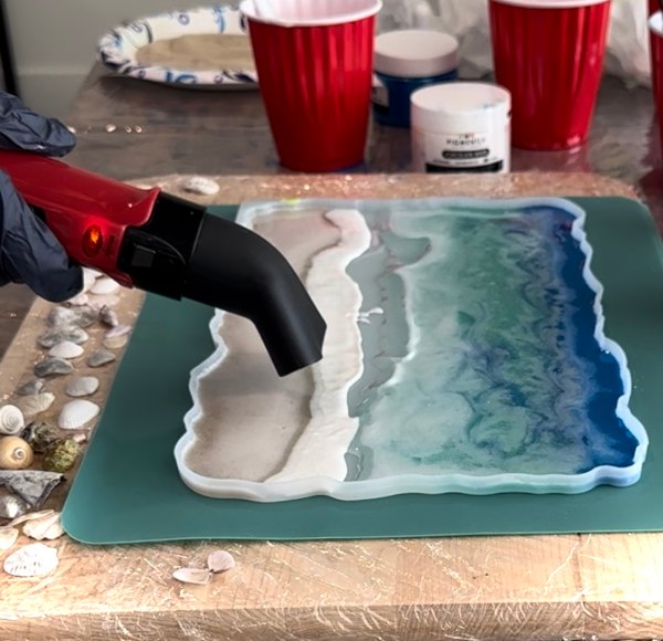 A heat gun being used to push epoxy resin layers around and blend them together to create the impression of ocean waves in an epoxy ocean project.