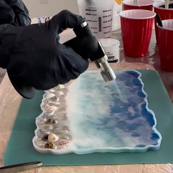 A torch being used to remove air bubbles from an epoxy ocean-themed project just before allowing it to cure.
