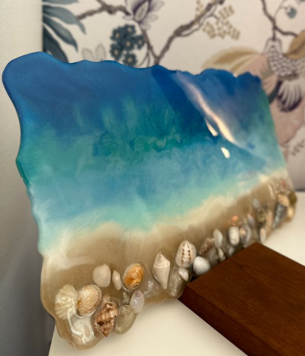 A finished epoxy resin ocean art piece standing on a desk against a wall.