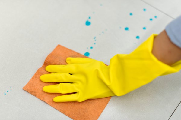 A hand wearing a rubber glove cleaning a tile surface.