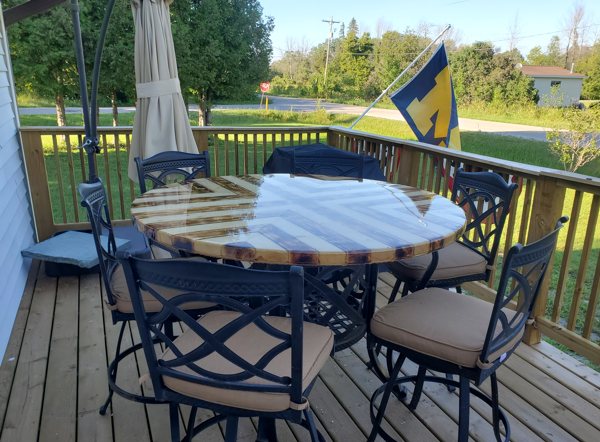 An outdoor wooden epoxy table top with several chairs around it.