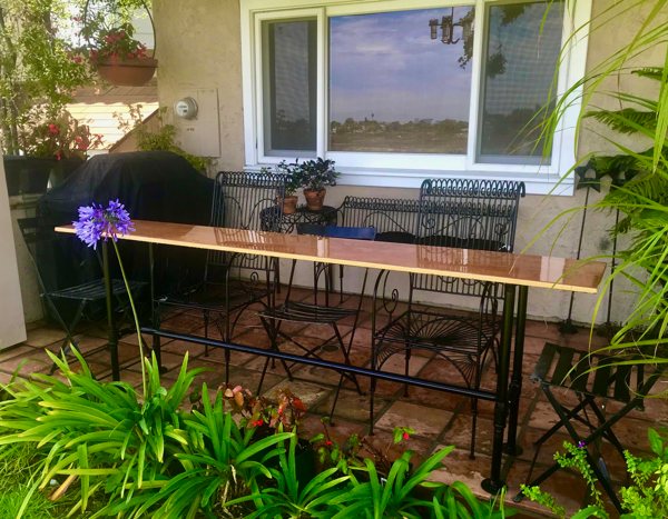 An outdoor epoxy wooden bar top, with different types of foliage in the foreground and a house behind it.