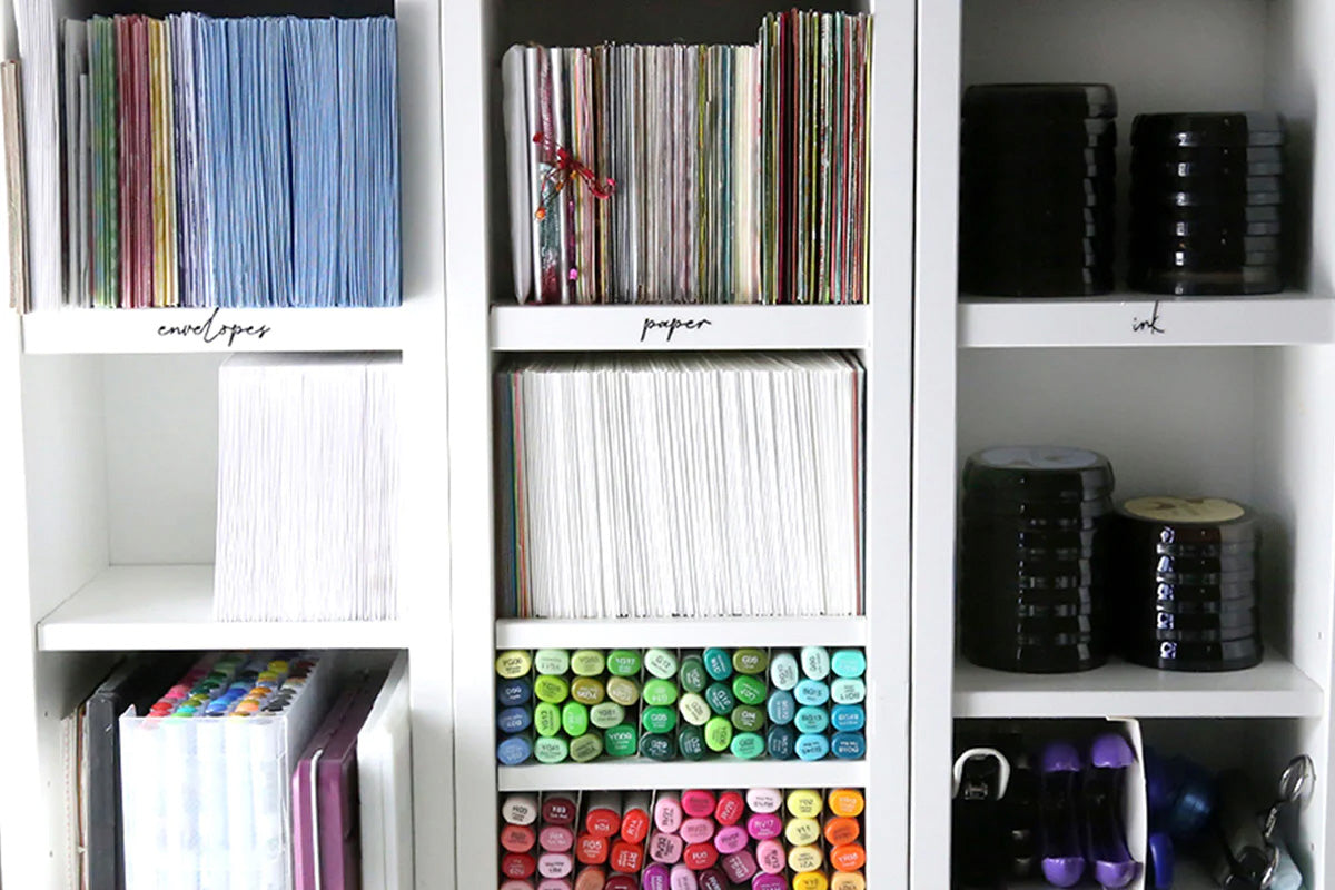A well-organized cabinet full of crafting supplies like cardstock, paper, dye ink pads, alcohol markers, and more