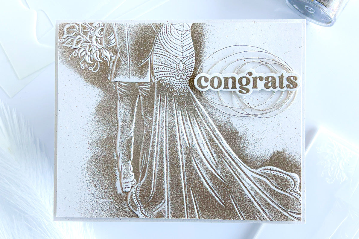 A monochromatic wedding card with an embossed image of the bride and groom, embellished with metallic thread
