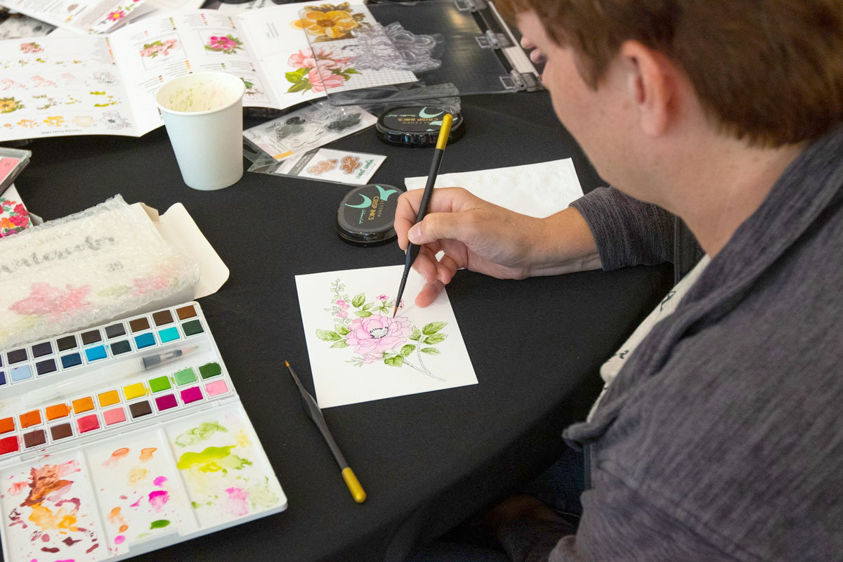 A guy coloring a floral card with Altenew's watercolor paints