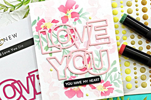 DIY Valentine's Day card with stencil flower art on the background and the words "love you" die-cut from pink cardstock