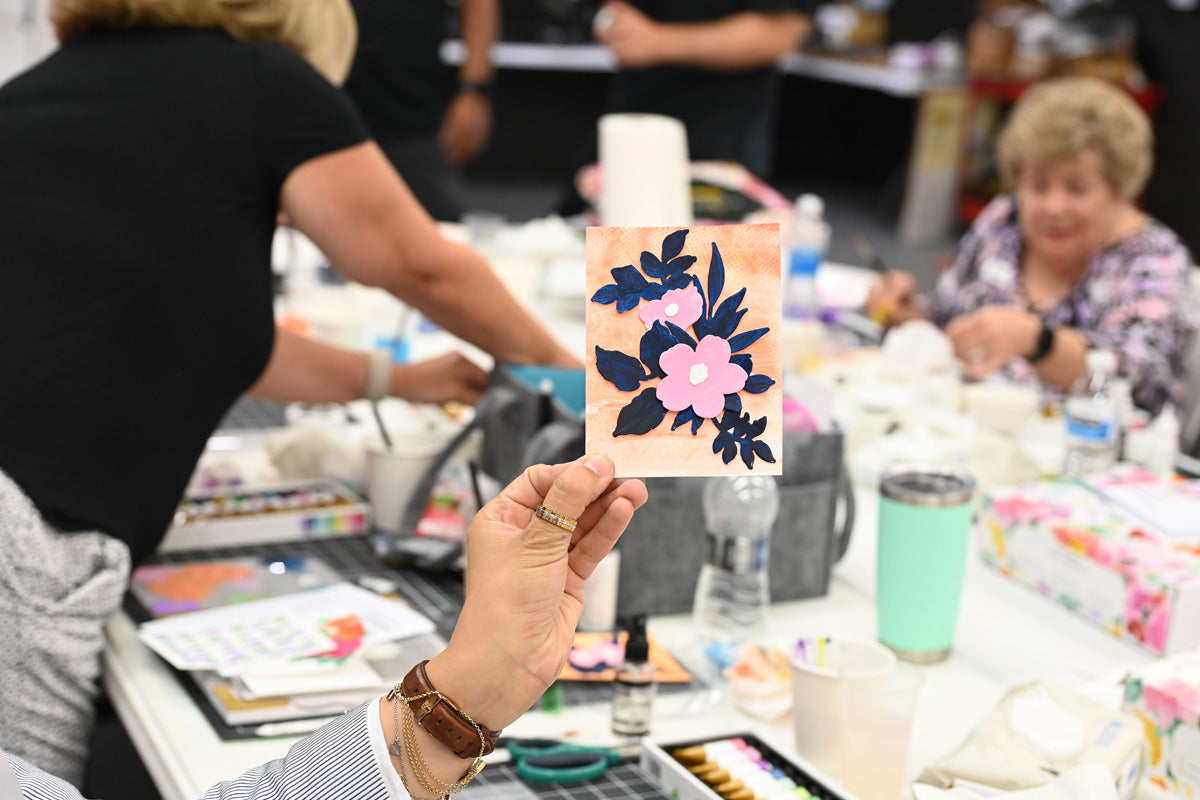 A crafter holding a handmade card in an in-person cardmaking workshop