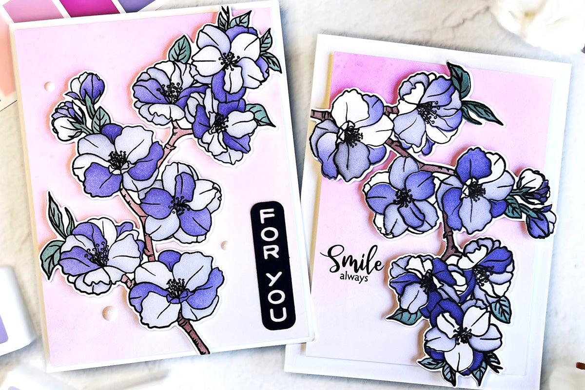 Two cards created with blue-colored sakura bloom die-cuts on a pink-tinged background, one card with a "for you" sentiment, and the other saying "smile always"