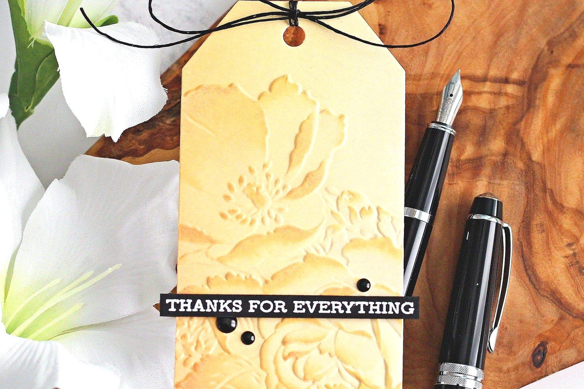 A gold tag with a 3D embossed floral background, with the sentiment "Thanks for everything", created with Altenew's pigment inks