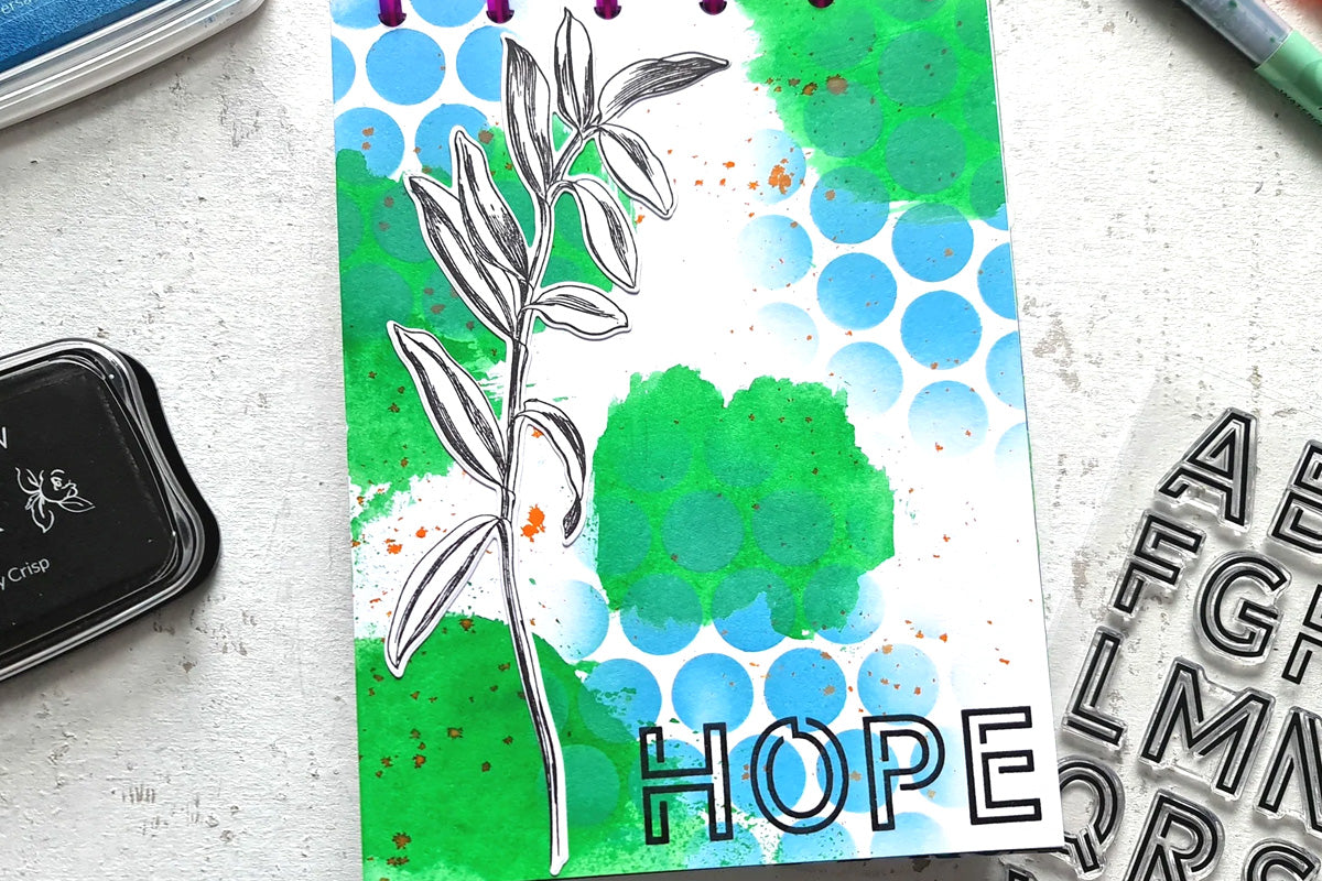 A journal page with the word "hope" on the bottom right corner, designed with  a blue-and-green honeycomb pattern, and a simple print of a stalk with some leaves off to one side, created with Altenew's pigment inks