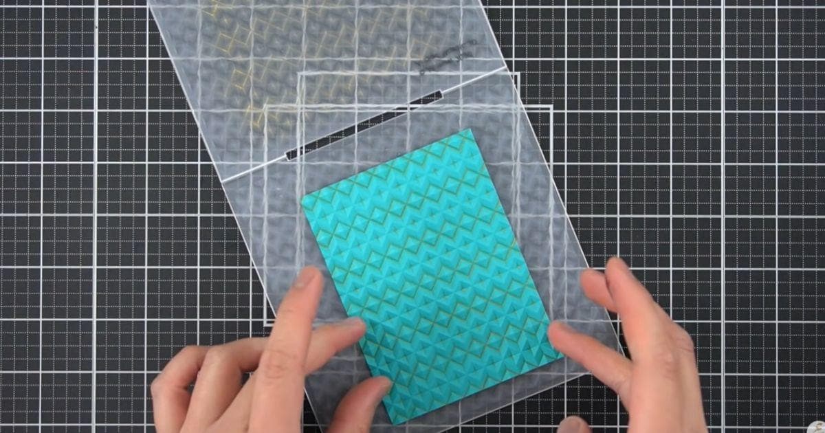 A flatlay shot of a crafter revealing an inked and embossed image on a panel of teal cardstock