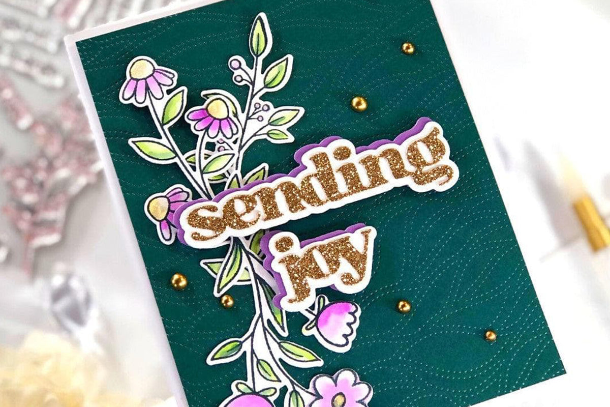 Handmade greeting card with a dark green 3D embossed background, floral die-cuts, and the sentiment "sending joy" cut out of glitter cardstock
