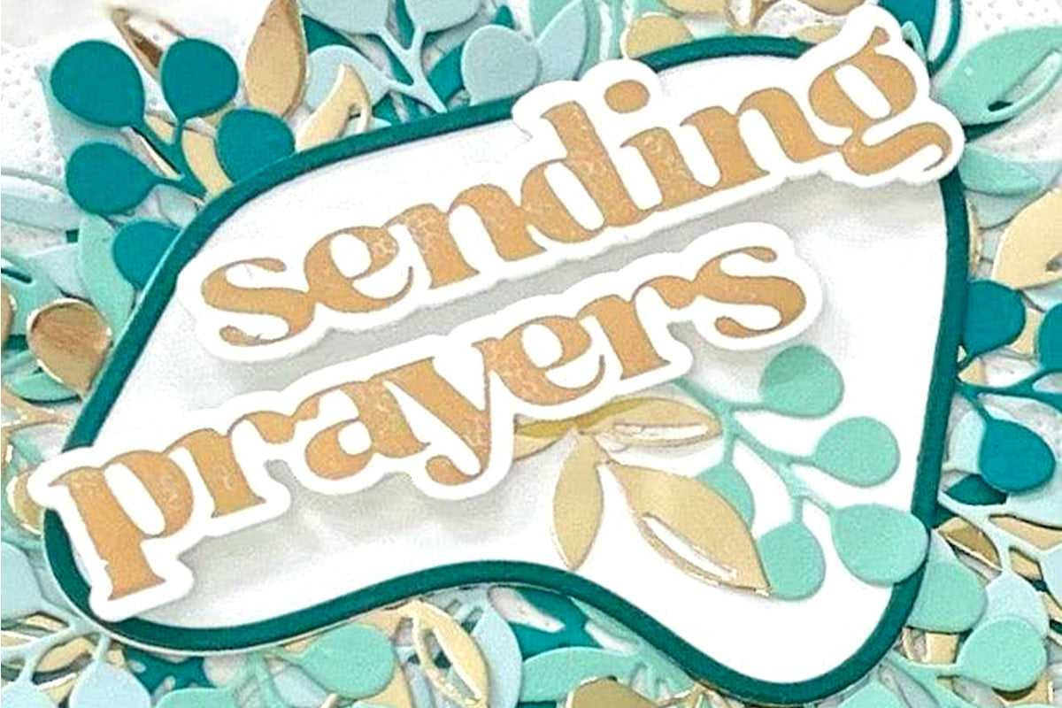 A close-up shot of a handmade sympathy card with die-cut flowers and foliage, and the sentiment "sending prayers"