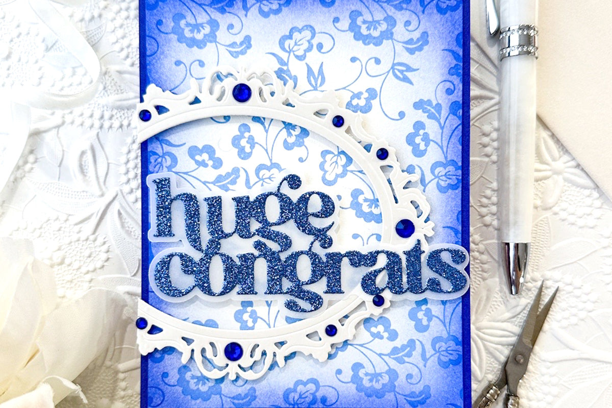 A congratulatory card with a blue floral background and the Sparkled Frame die-cut decorated with Deep Sea Sapphire Gem Sparkles