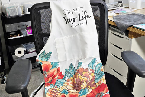 A white crafting apron with floral designs from Altenew, draped over an office chair
