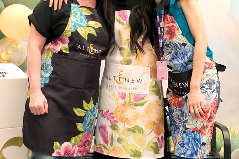 A mid-shot of 3 ladies wearing the Altenew crafting aprons in various colors