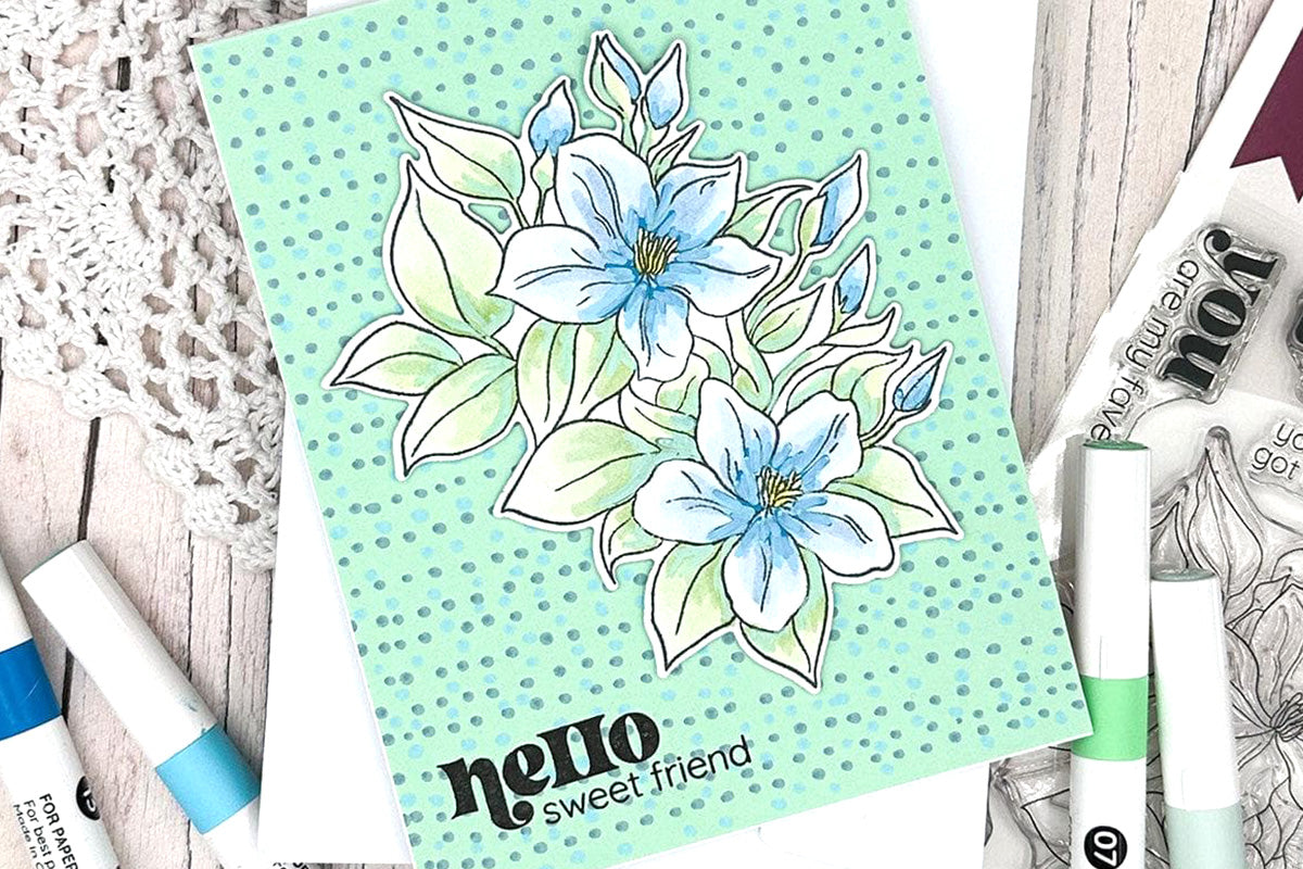 A greeting card with blue flowers as focal points and a teal-colored background, decorated with accents from Artistry by Altenew's Acrylic Marker 24 Color Set - Vol. 1